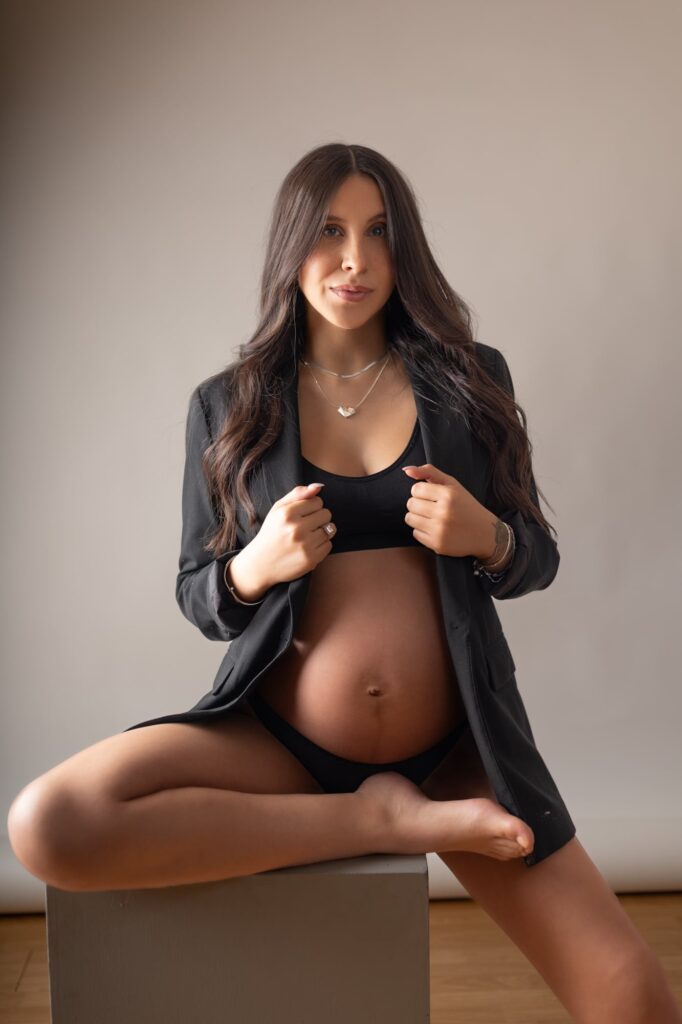 Retrato en primer plano de una futura mamá con un maquillaje sutil y peinado elegante, sonriendo con confianza mientras posa de manera relajada y natural