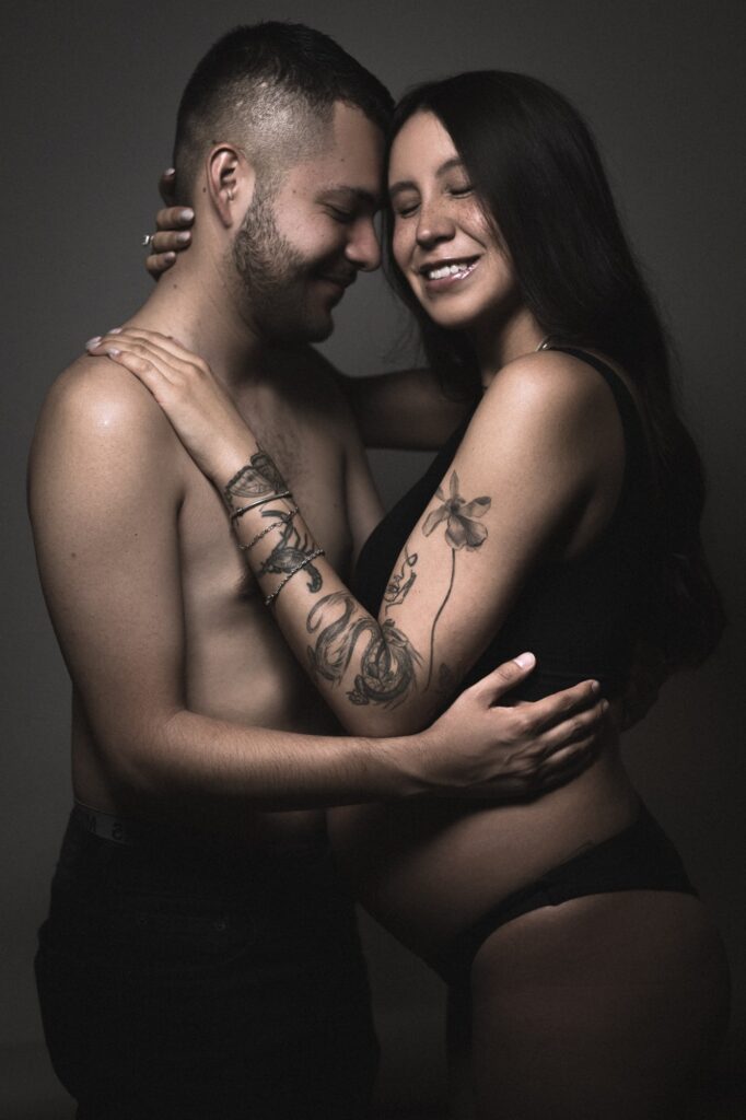 Retrato íntimo de una pareja abrazada, el hombre con la cabeza apoyada en el hombro de su esposa embarazada, reflejando el amor y la conexión que comparten.