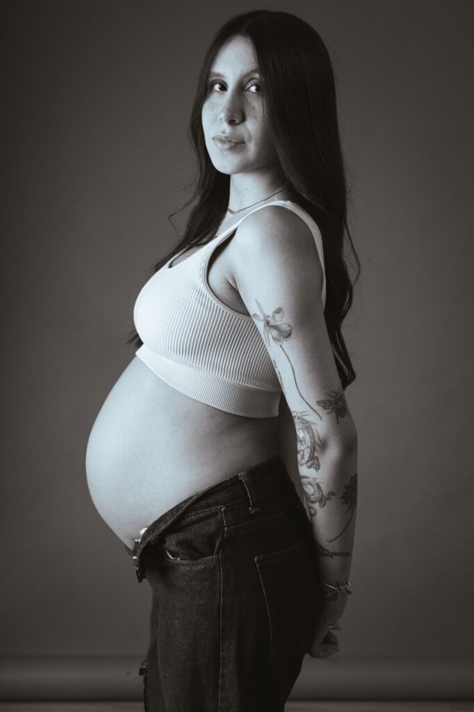 Retrato en primer plano de una futura mamá con un maquillaje sutil y peinado elegante, sonriendo con confianza mientras posa de manera relajada y natural.